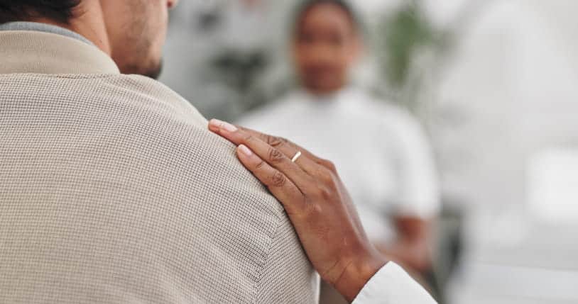 A hand resting on a person's shoulder as they're being consoled after a tragic event. 