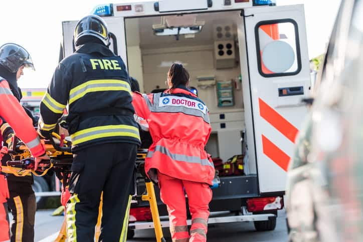 Paramedics and firefighters are loading a stretcher into the back of an ambulance after a catastrophic injury. 